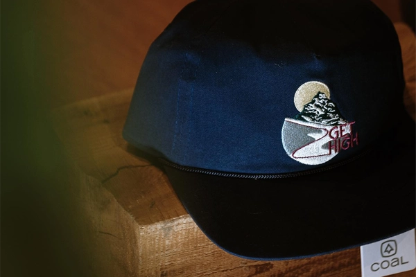 Navy cap with mountain branding displayed on wooden block at NYLA Fresh Thread's Nanaimo store